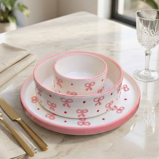 Set of ceramic bowls with pink bow design on a marble table.