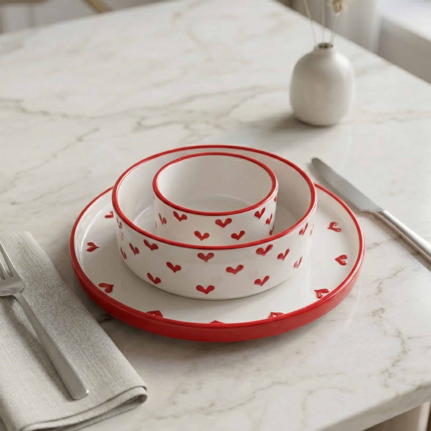Set of white bowls with red heart patterns on a marble table.