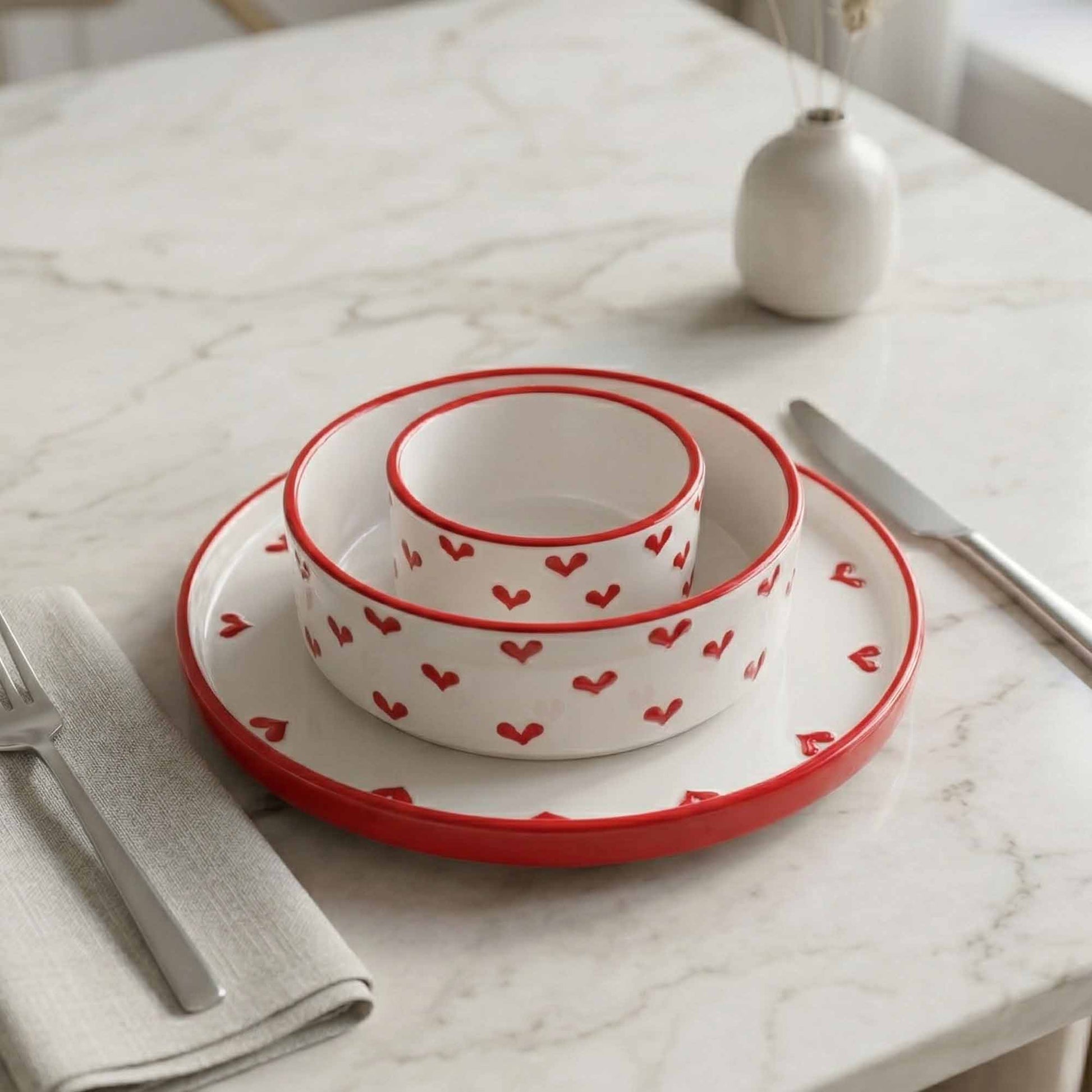 Set of white bowls with red heart patterns on a marble table.