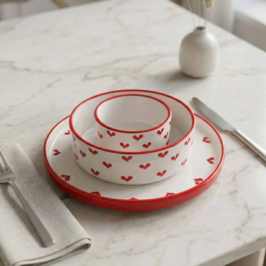 Set of white bowls with red heart patterns on a marble table.