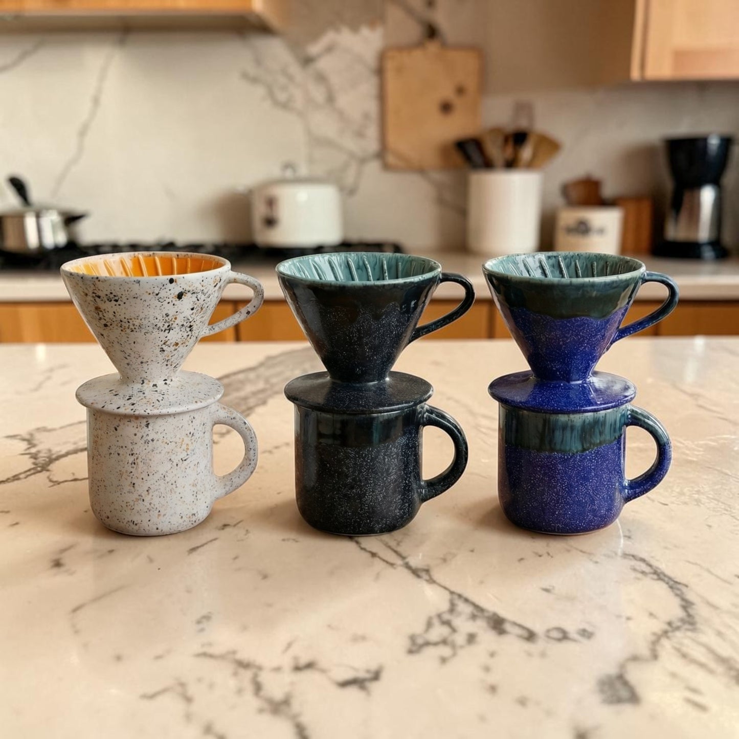 Four ceramic coffee filters and mugs stacked on a marble countertop with a kitchen background.