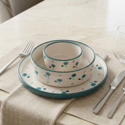 Ceramic dinnerware set with floral pattern on a table with cutlery and glass.