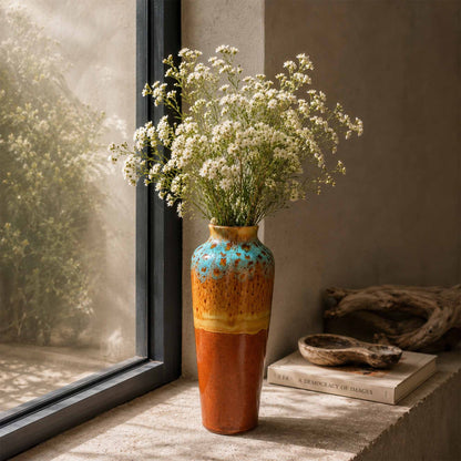Ceramic vase with white flowers on a windowsill next to books and driftwood.