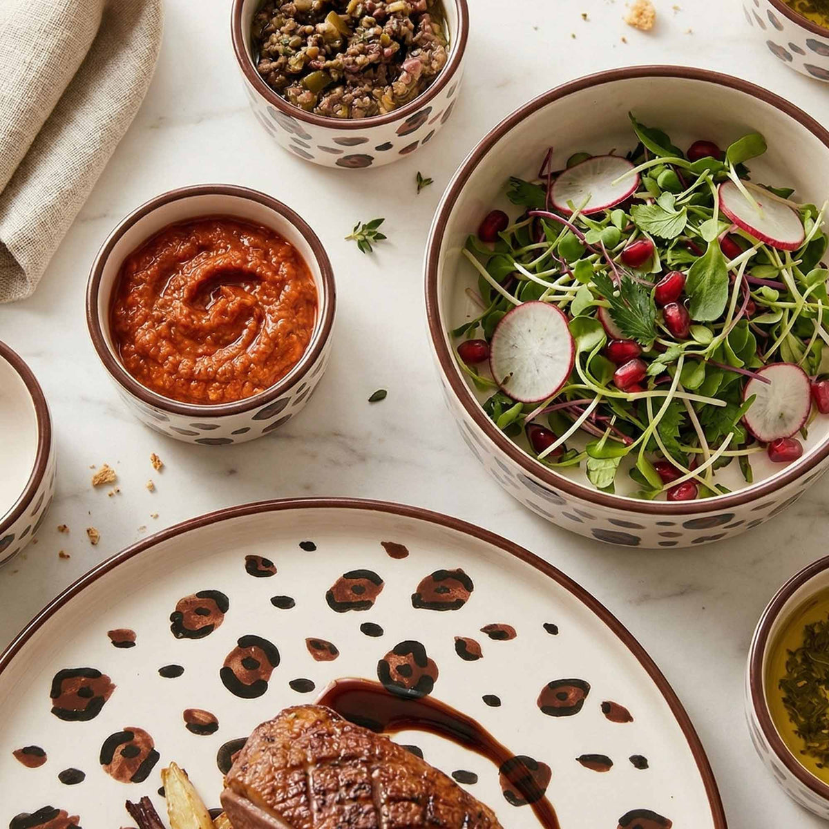 Dinner setting with a plate of meat, bowls of salad and sauce on a marble surface.