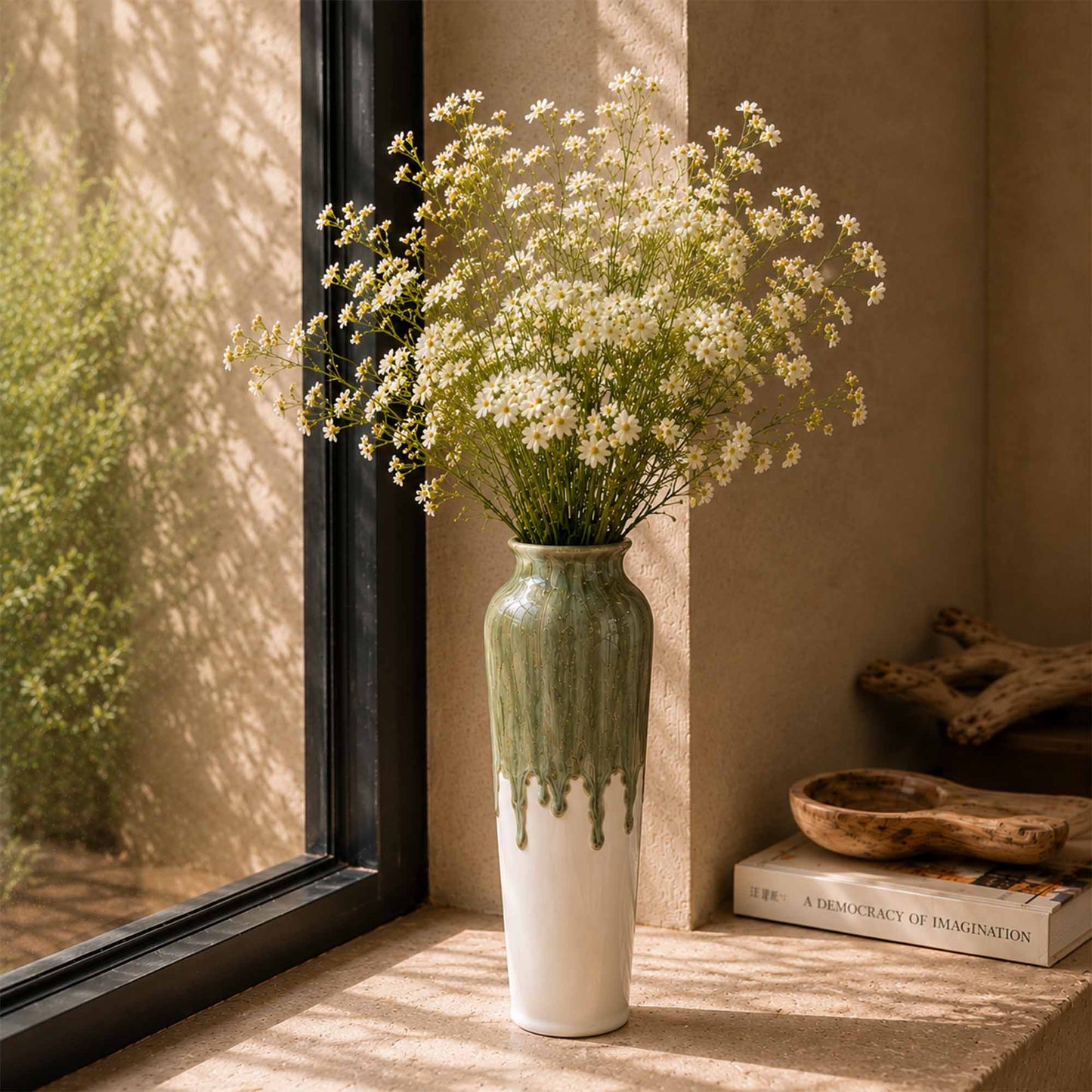 White vase with green base holding a bouquet of white flowers on a windowsill.