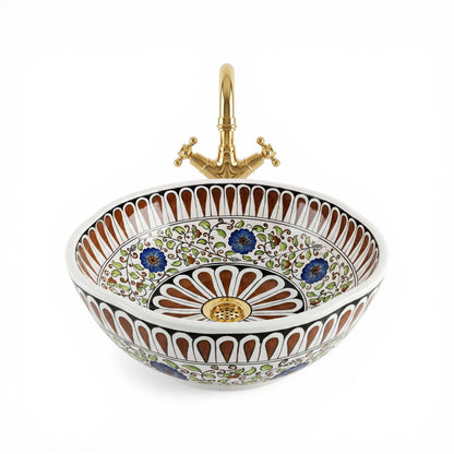 Decorative ceramic sink with floral patterns and a gold faucet on a white background