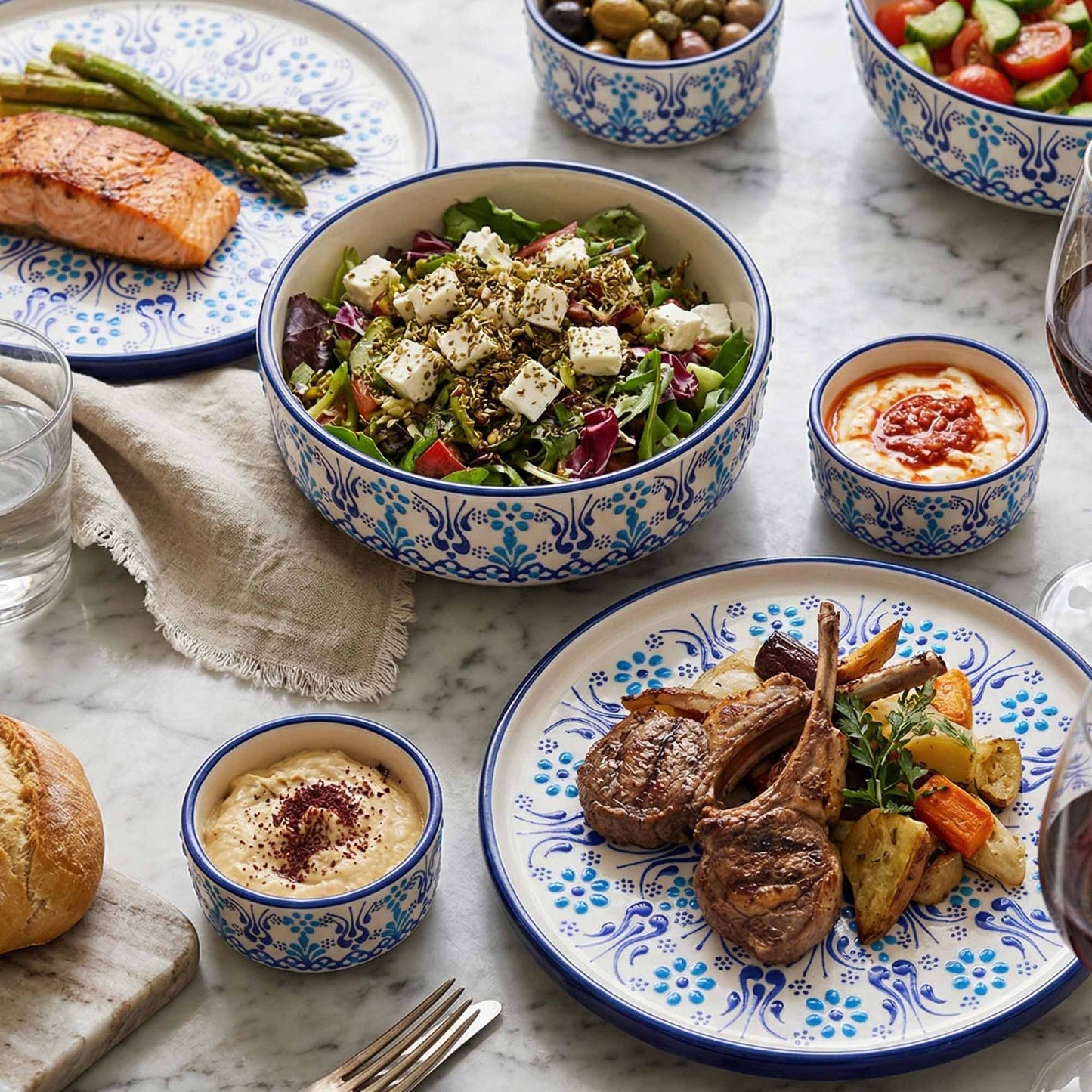 Dinner table with plates of food including salad, roasted meat, and bread, set on a marble surface.