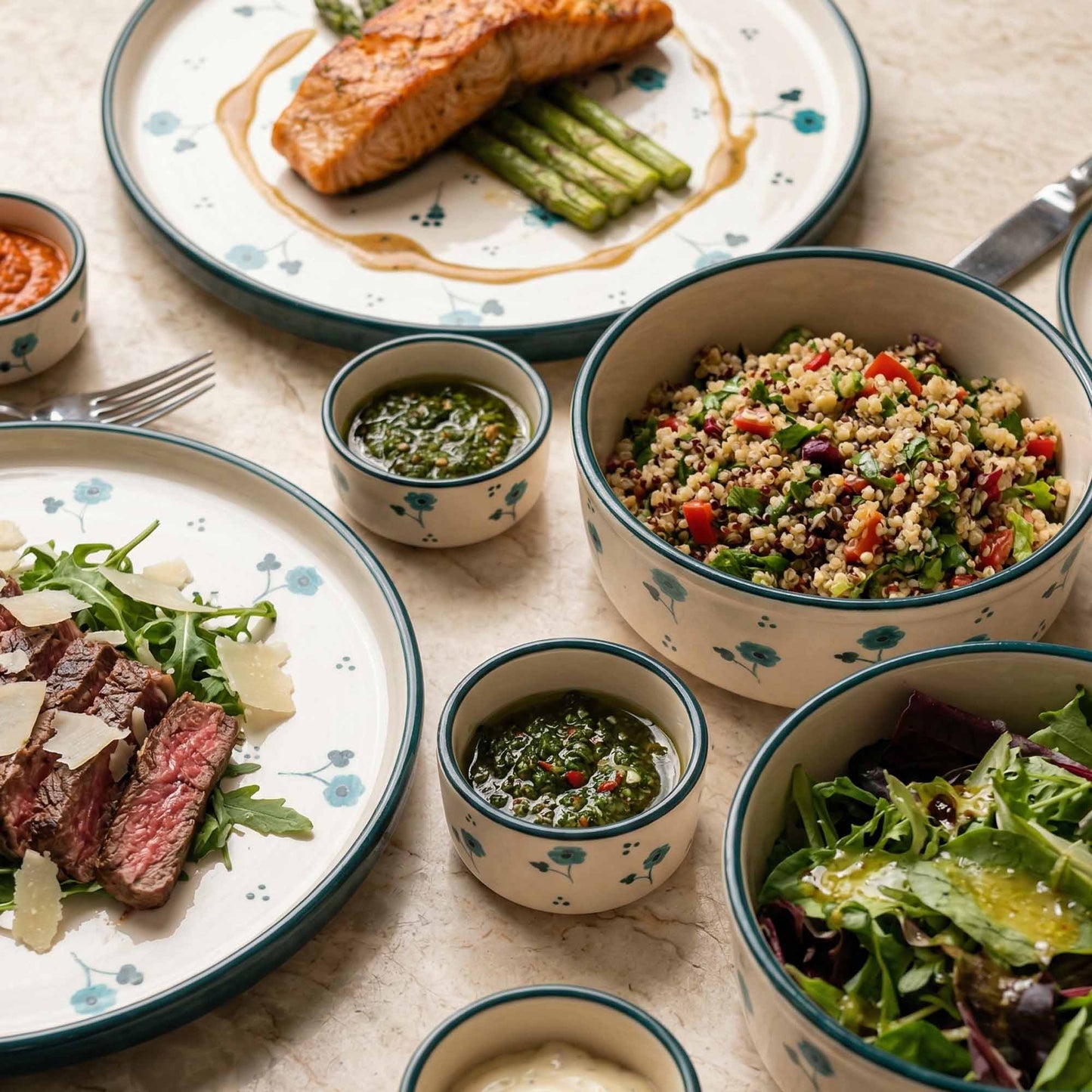 Dinner setting with plates of salmon, salad, and bowls of quinoa salad and green sauce on a table.
