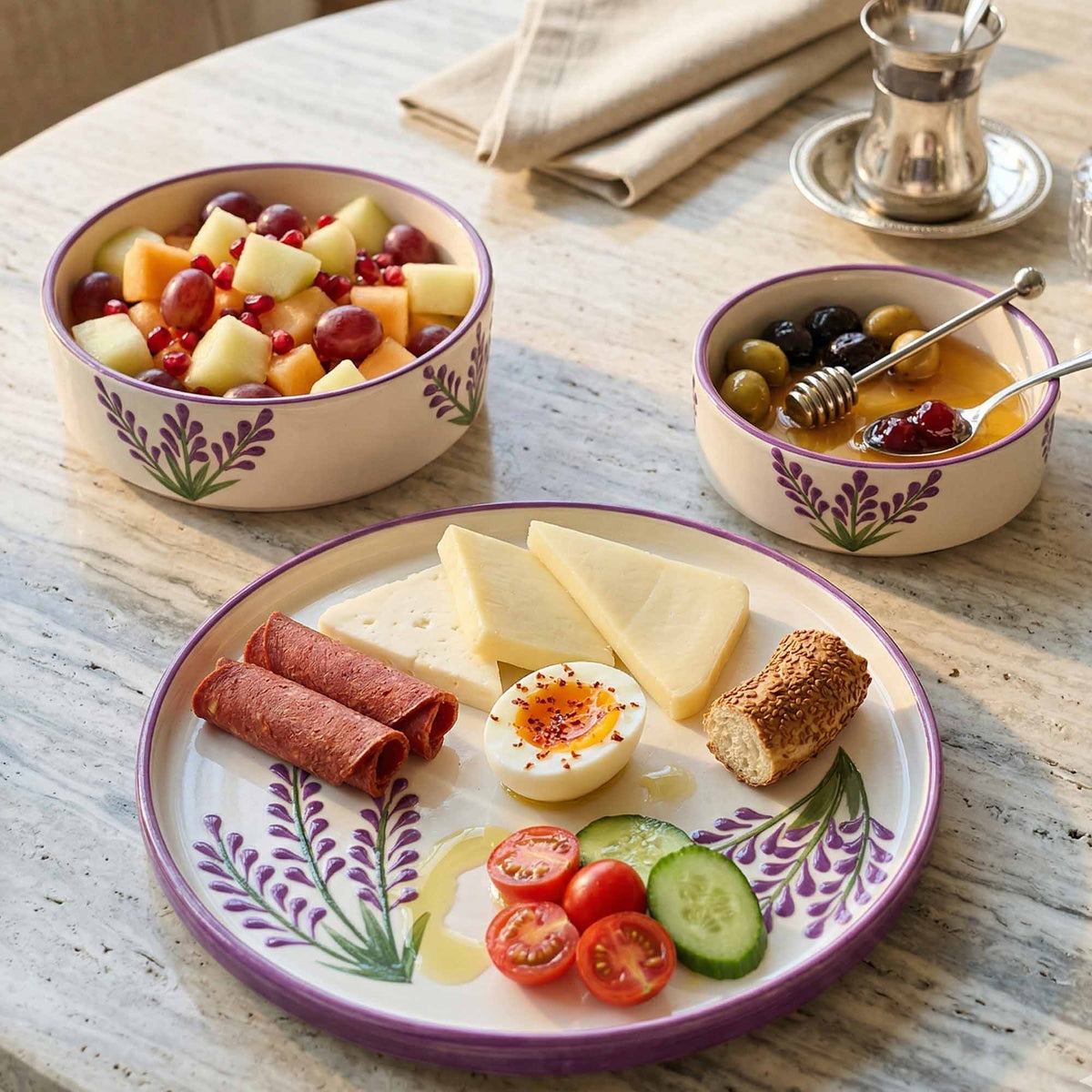 Assorted food items on a decorative plate with two bowls of fruit and olives on a wooden table.