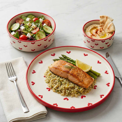 Dinner setting with salmon dish, salad, and hummus on a heart-patterned plate and bowls.