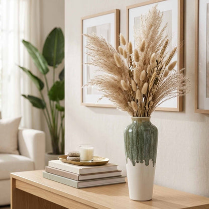 Decorative ceramic vase with dried plants on a wooden table in a living room setting.