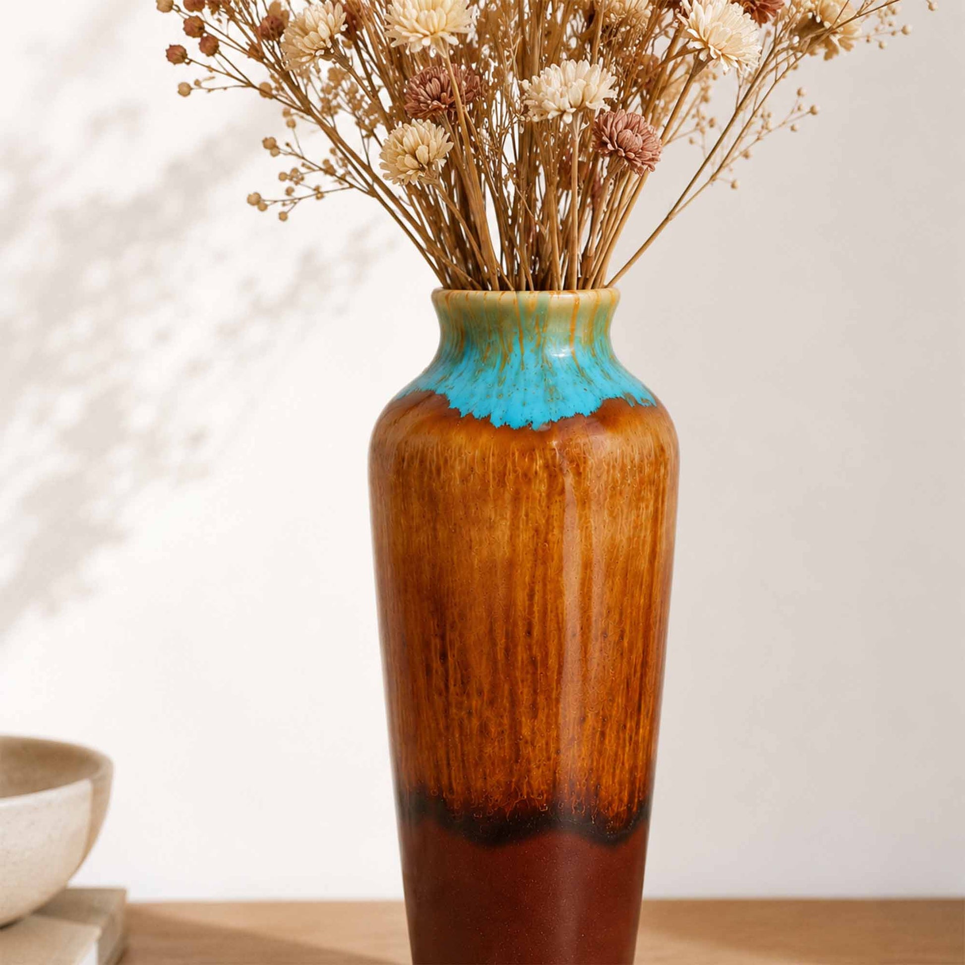 Tall ceramic vase with a gradient finish holding dried flowers on a neutral background