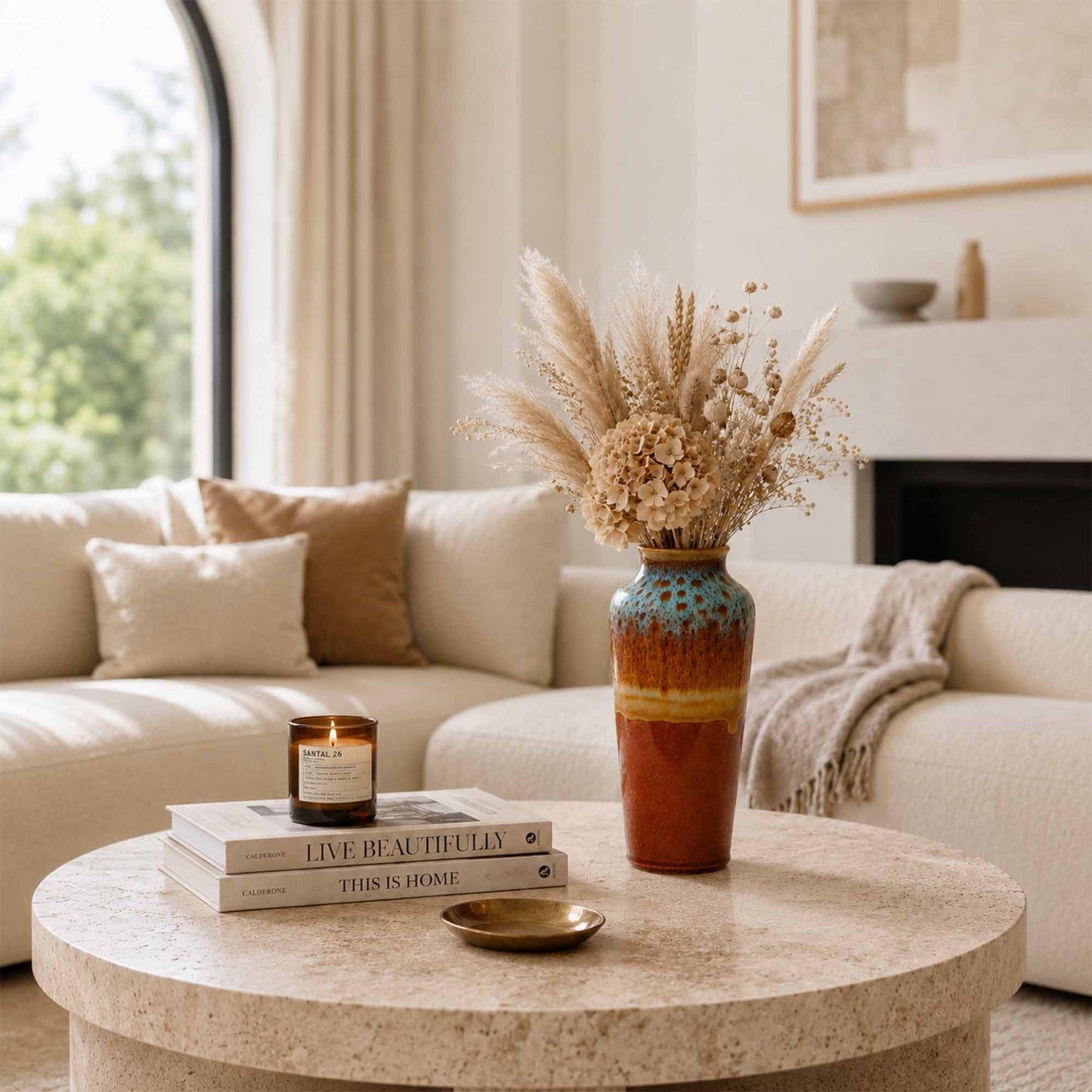 Living room with a round coffee table featuring a ceramic vase with dried flowers, books, and a candle.