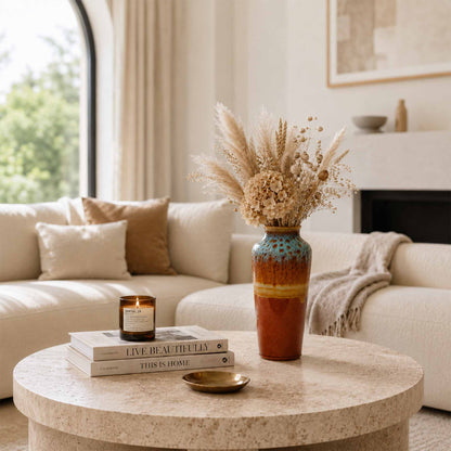 Living room with a round coffee table featuring a ceramic vase with dried flowers, books, and a candle.
