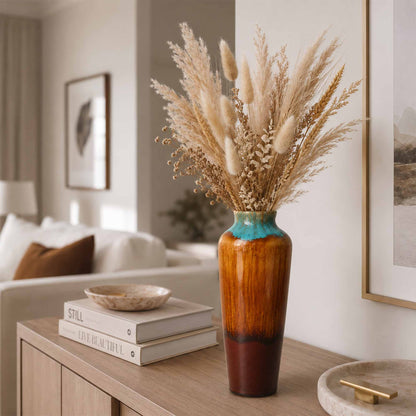 Decorative ceramic vase with dried plants on a wooden side table in a living room.