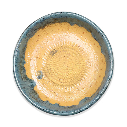 Ceramic garlic grater bowl with a textured blue rim containing a beige substance on a white background