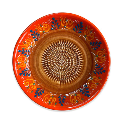 Decorative ceramic garlic grater bowl with orange rim and intricate brown center on a white background