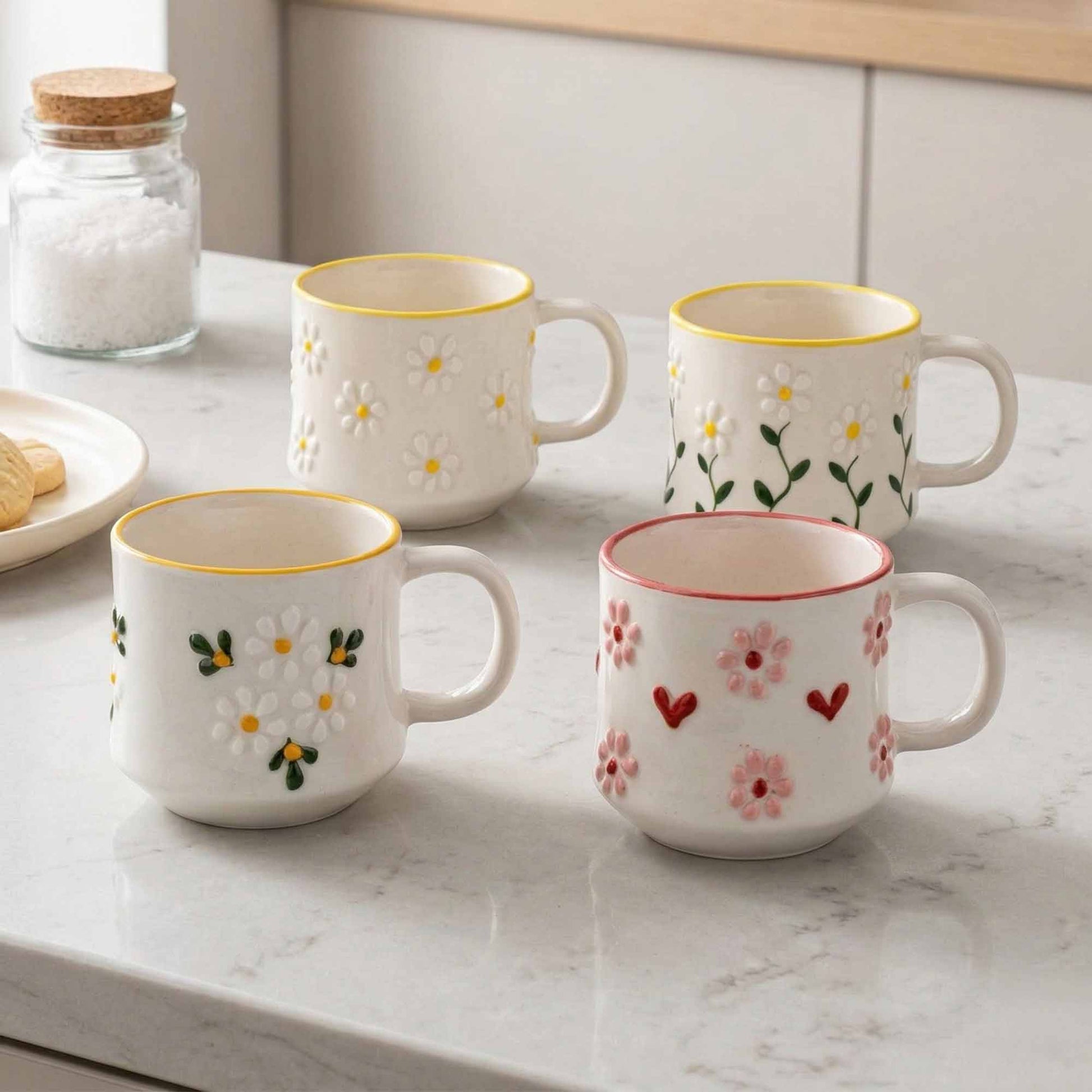 Four ceramic mugs with floral designs on a marble countertop.