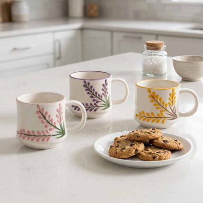 Three mugs with floral designs on a kitchen counter with a plate of cookies.