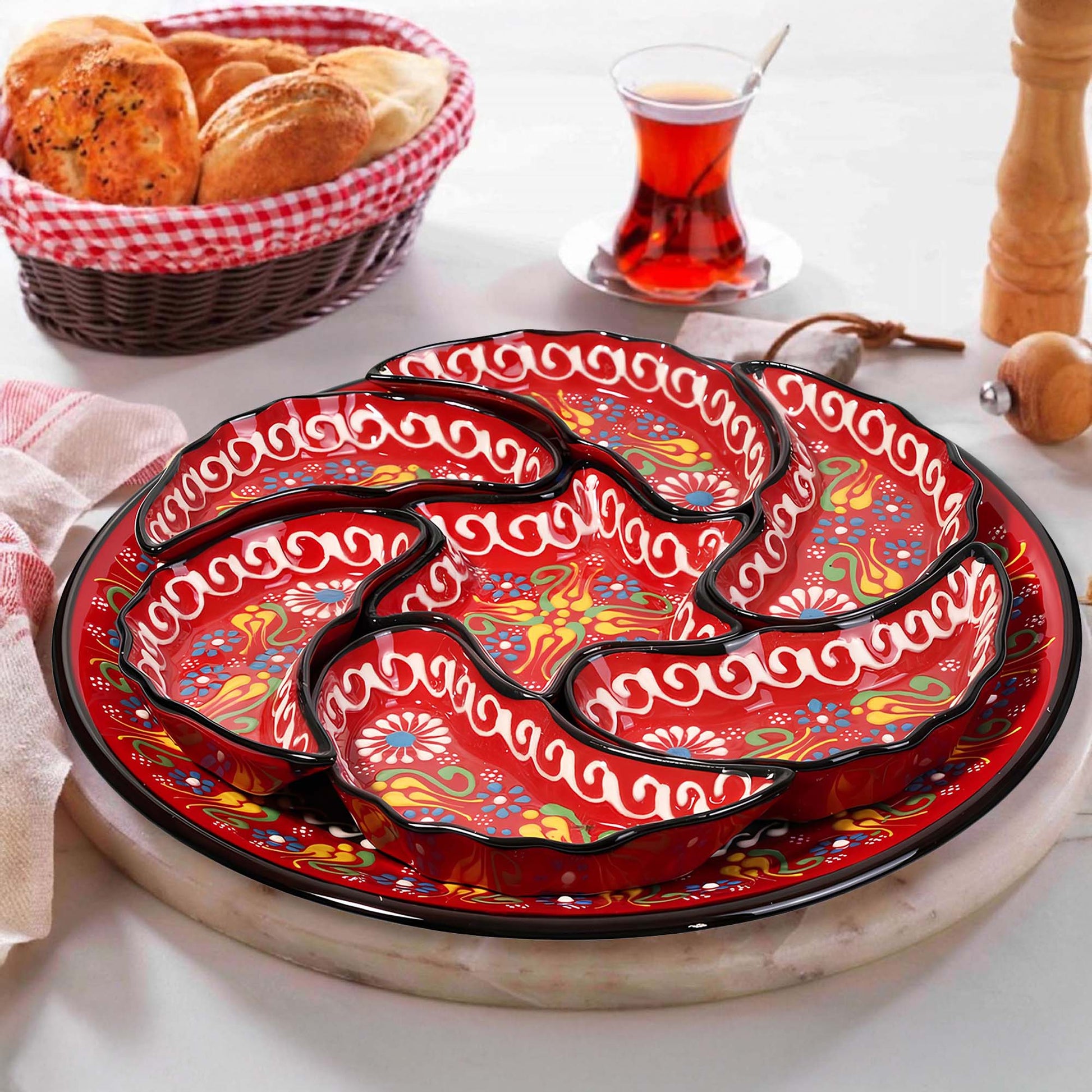 Decorative red snack serving tray set with floral patterns on a white surface, accompanied by a basket of bread and a glass of tea.