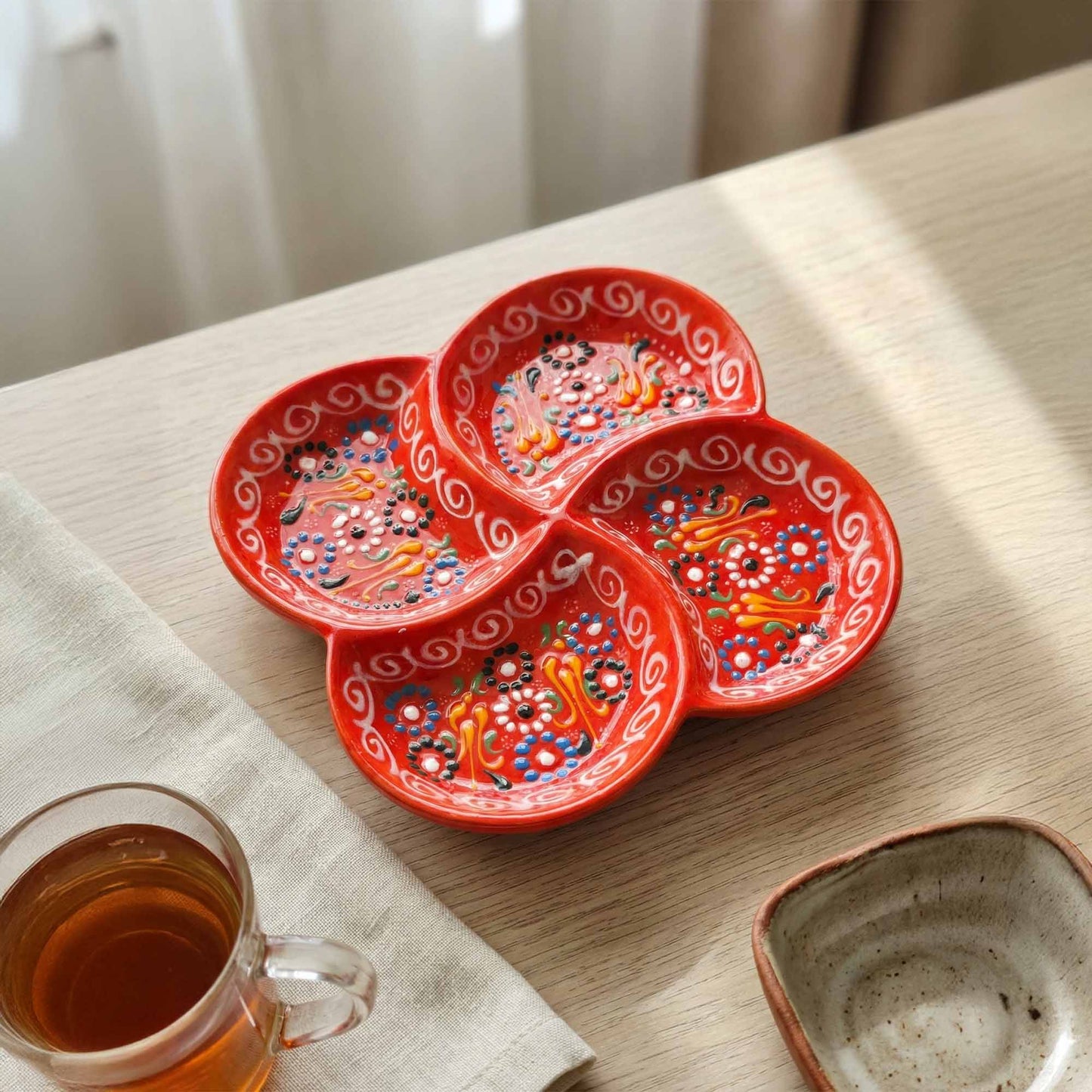 Red decorative plates with colorful patterns on a wooden table next to a glass of tea.