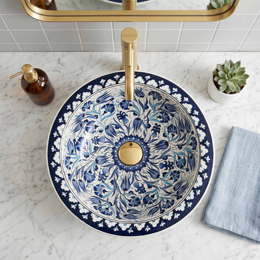 Decorative blue and white floral-patterned sink with gold faucet on a marble countertop.