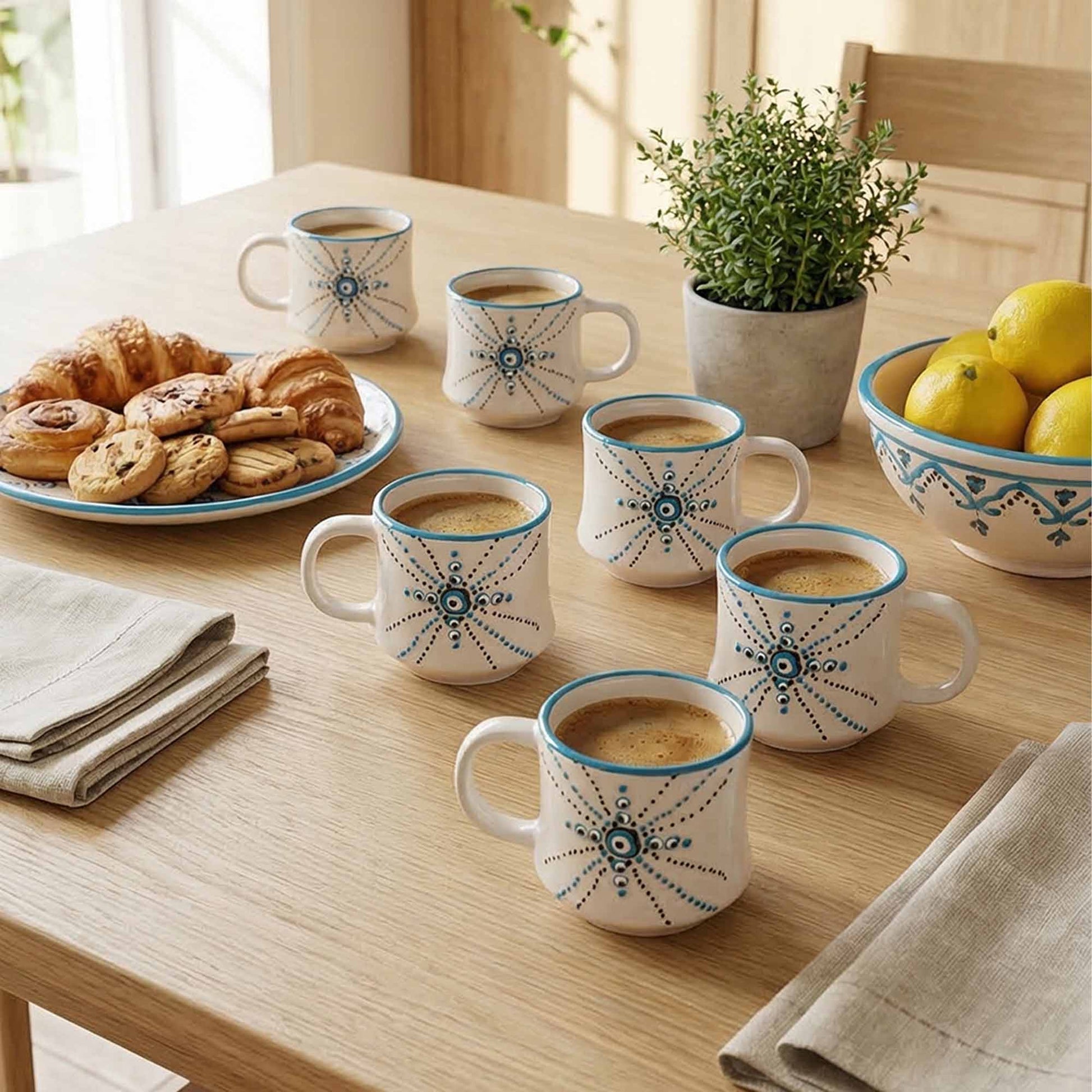 Set of coffee mugs with decorative patterns on a table with pastries and lemons.