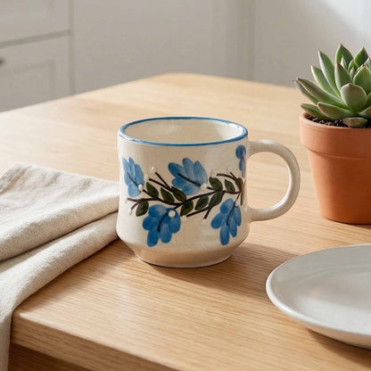 Ceramic mug with floral design on a wooden table with a potted plant and plate.