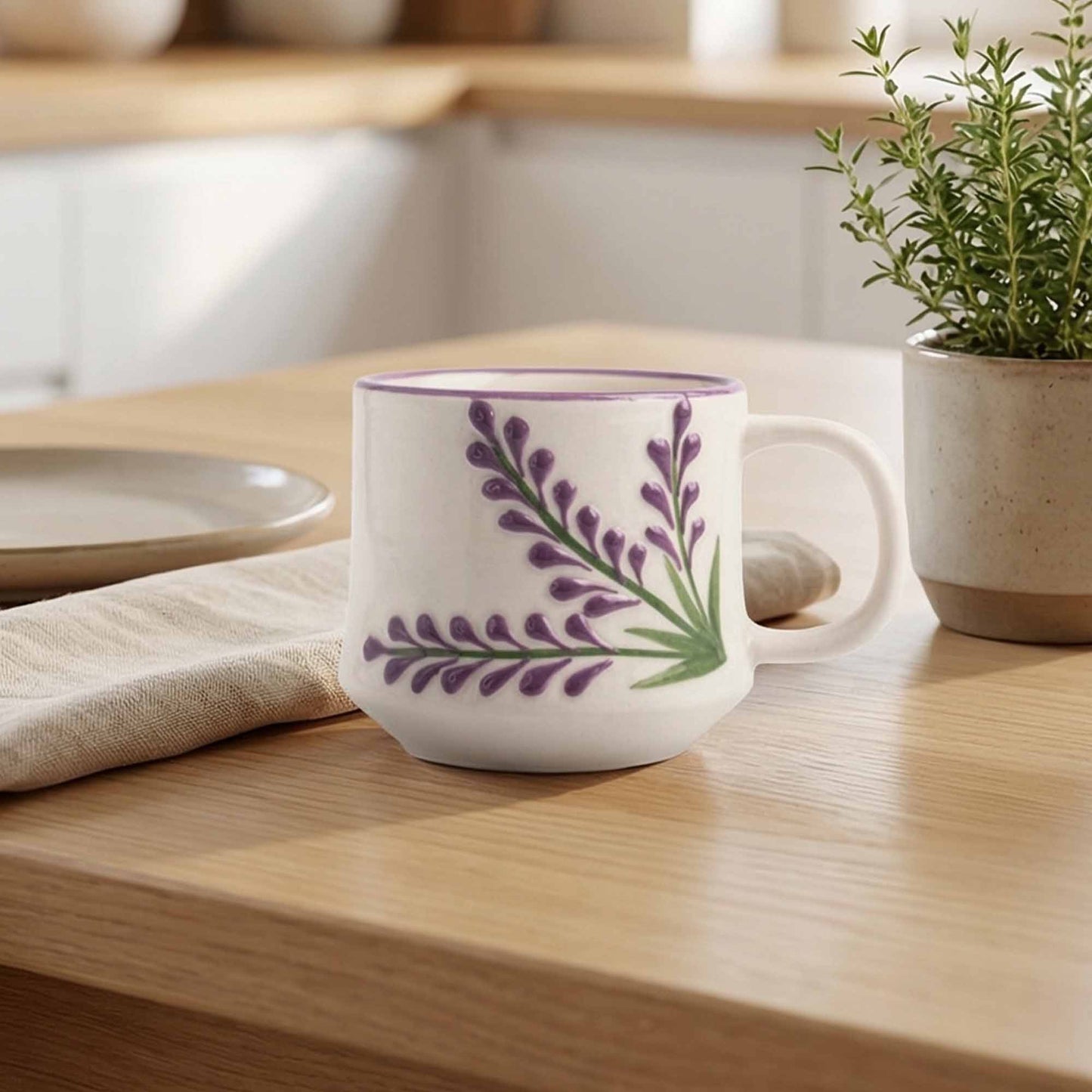 White mug with purple floral design on a wooden table with a plant and plates in the background