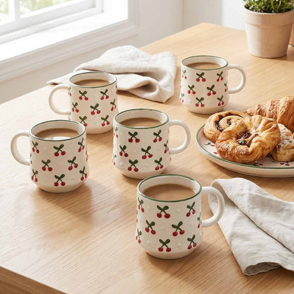 Set of coffee mugs with cherry design on a wooden table with pastries.