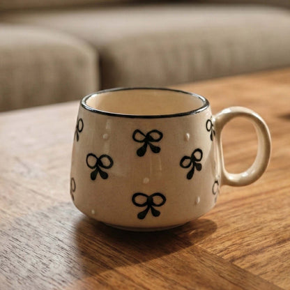 Beige mug with black bow patterns on a wooden surface