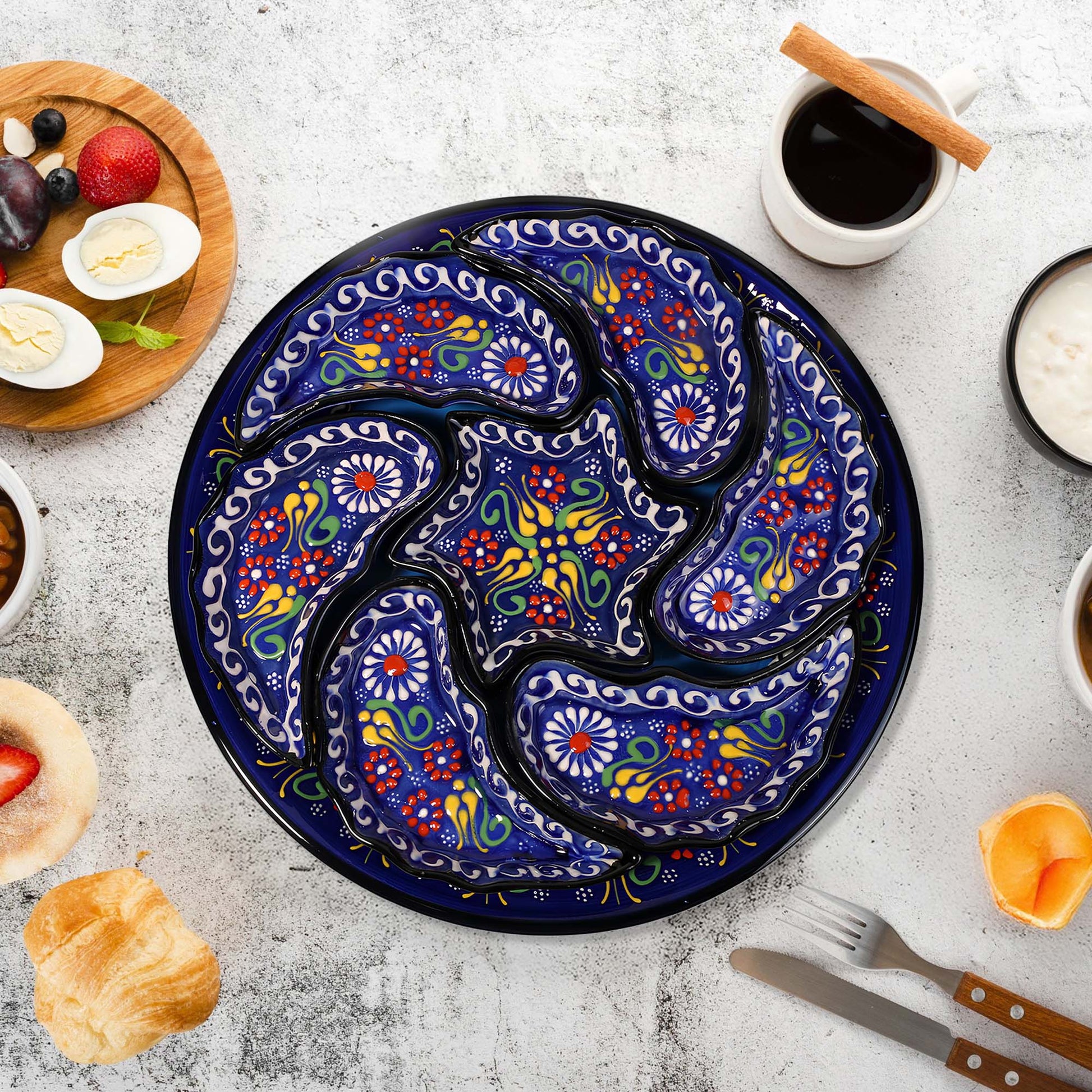 Decorative ceramic snack serving tray set with floral patterns on a table with food items and cutlery.