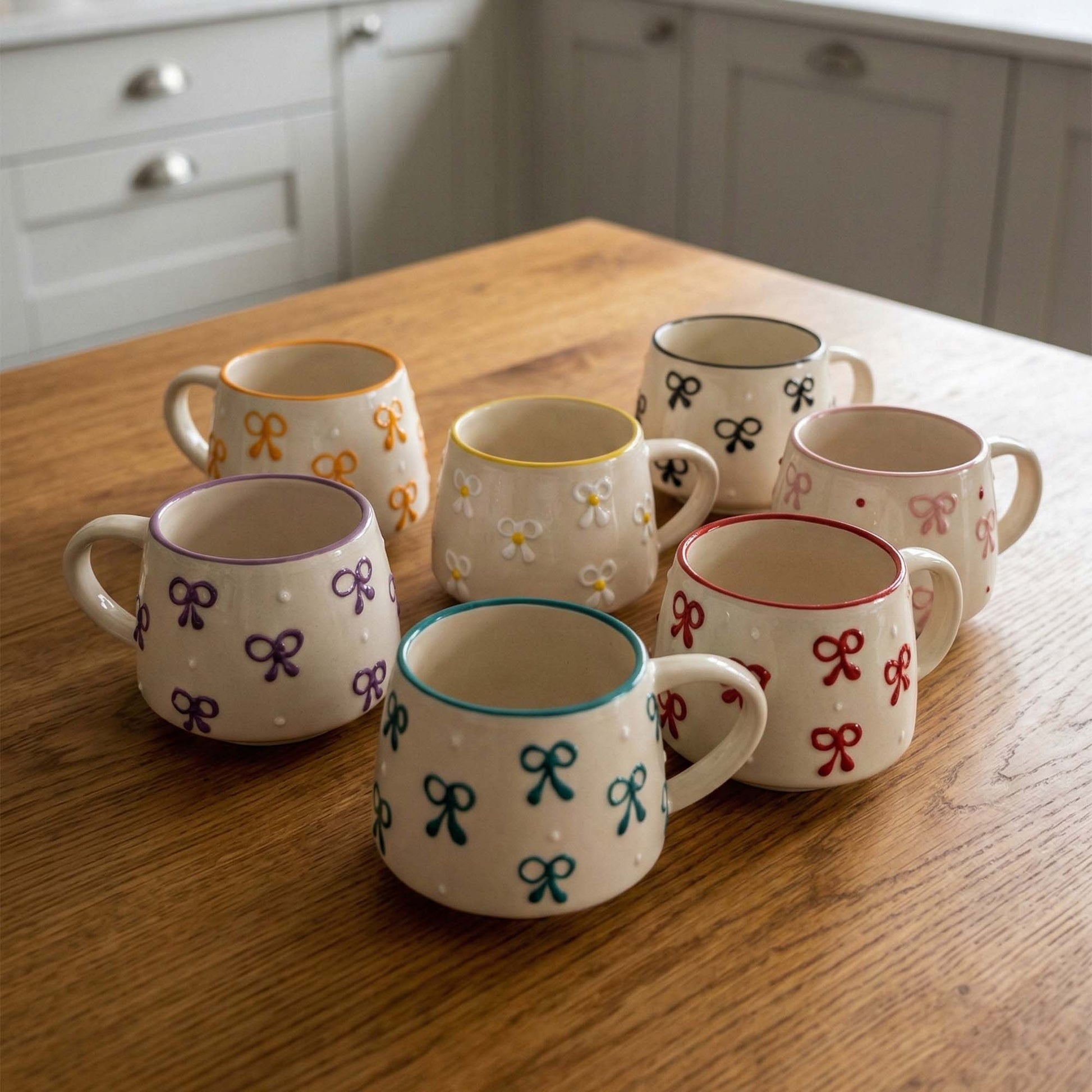 Set of ceramic mugs with colorful bow designs on a wooden table.