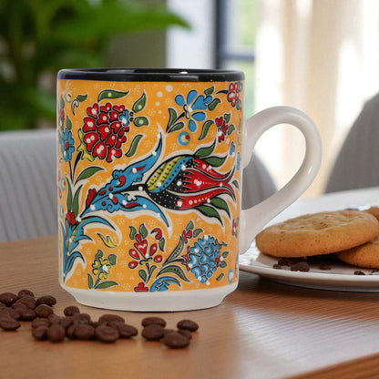 Colorful coffee mug with floral and bird design on a table with cookies and coffee beans.