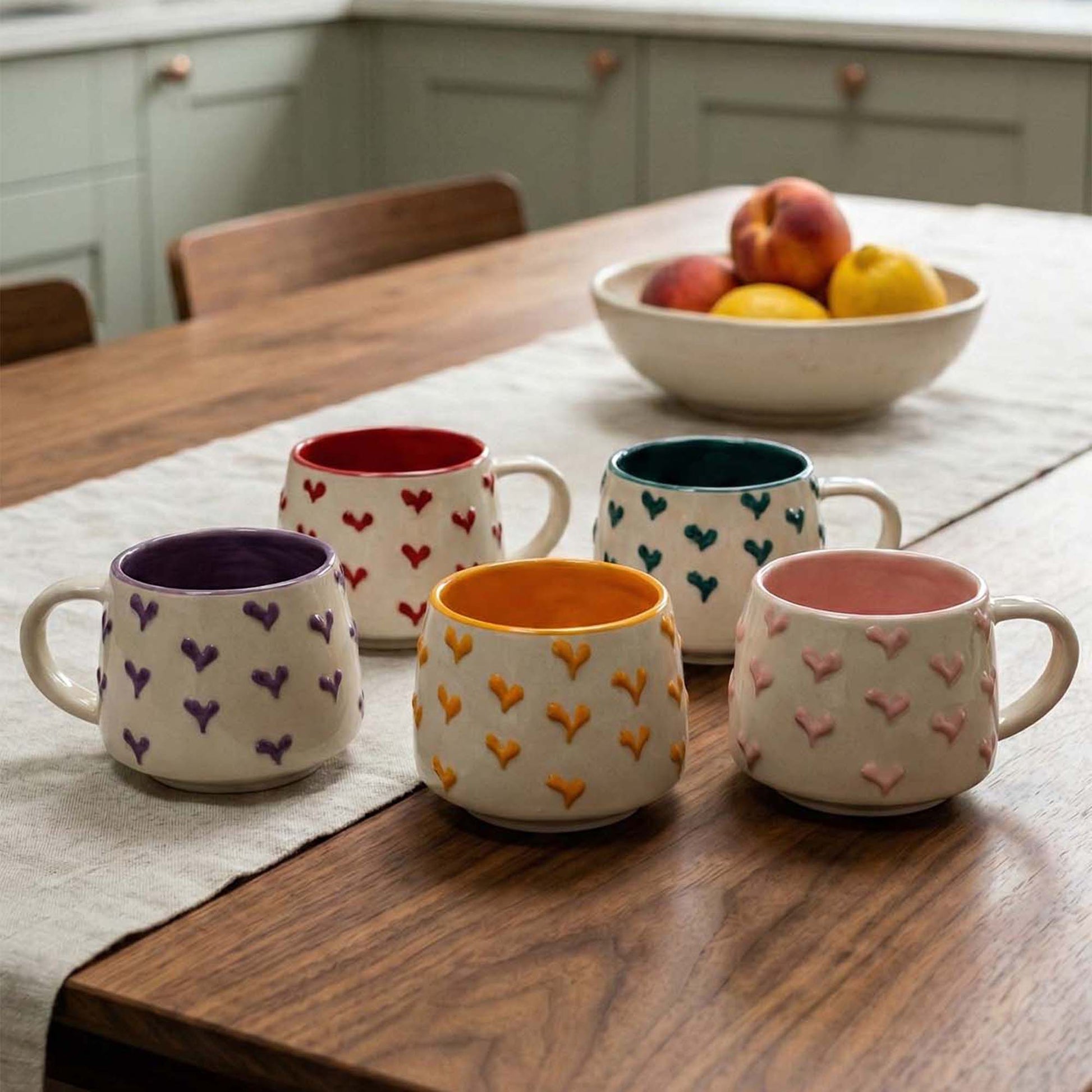 Set of colorful ceramic mugs with heart patterns on a wooden table.