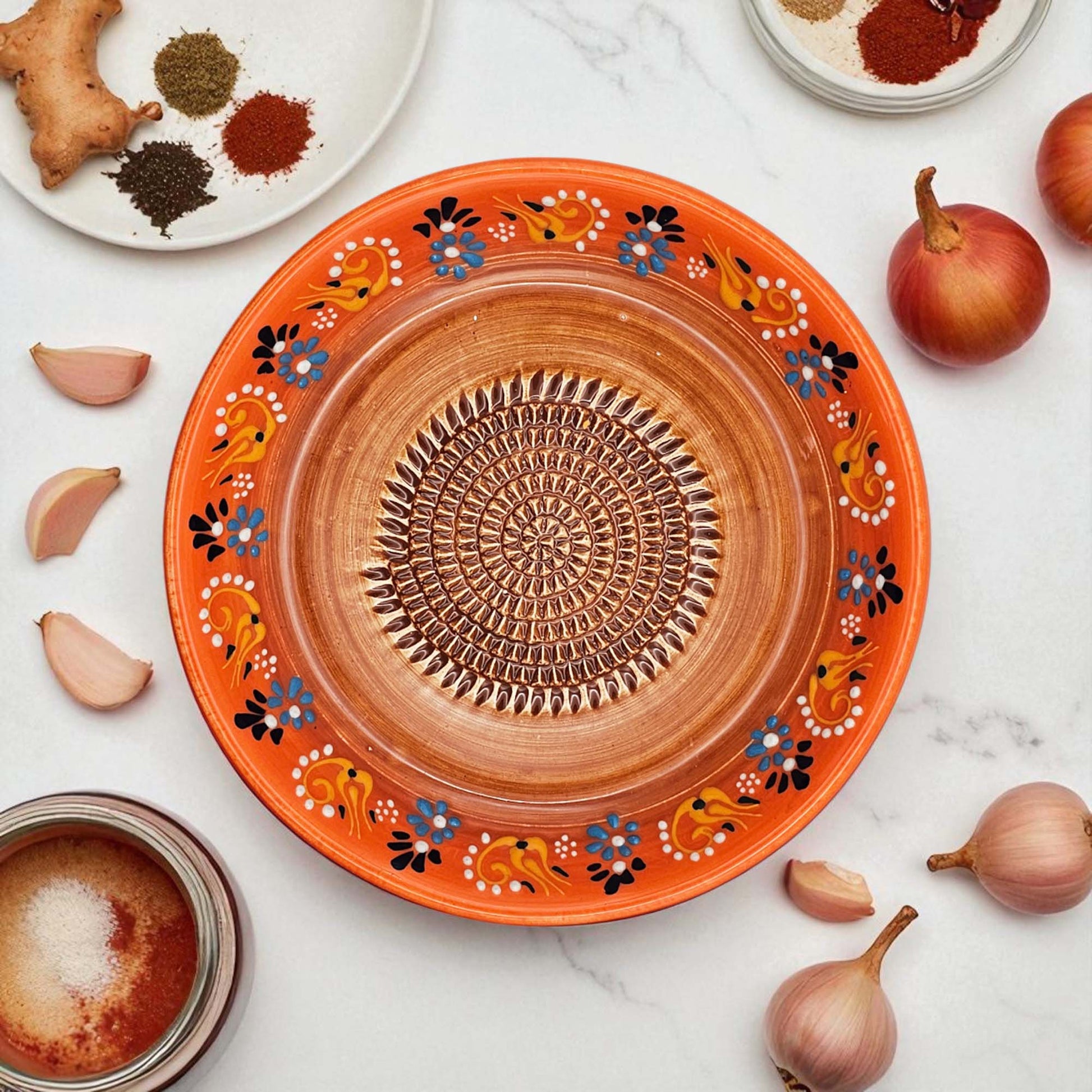 Decorative ceramic garlic grater bowl with floral patterns on a white surface with ingredients.