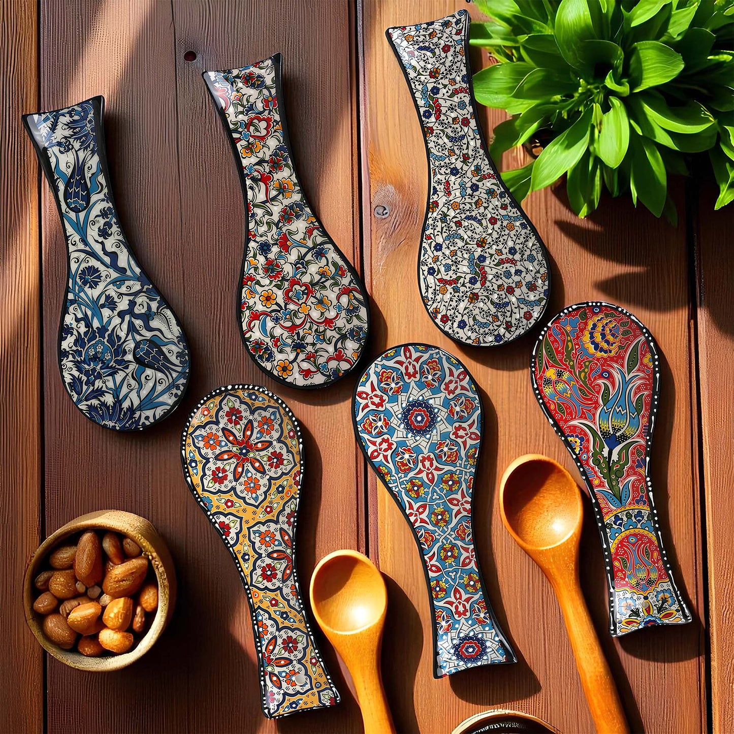 Decorative spoon rests with floral patterns on a wooden surface with a plant and bowl of nuts.