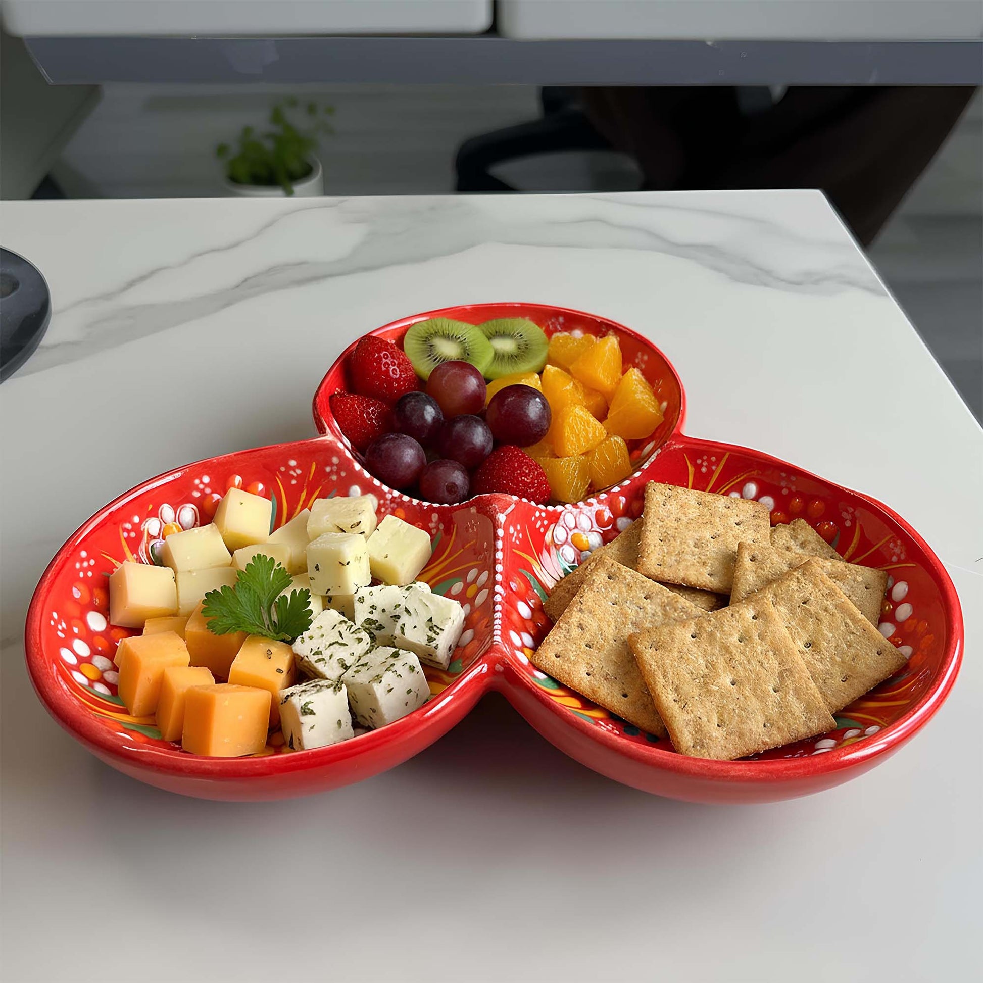 Red divided dish with fruits, cheese, and crackers on a white surface
