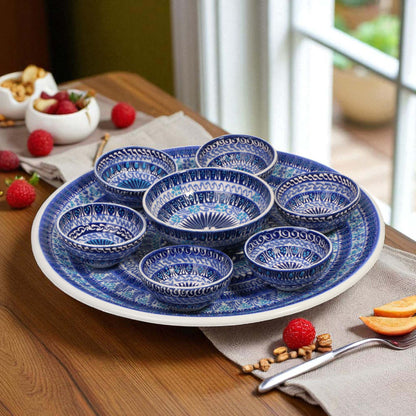 Set of blue ceramic bowls on a white plate with fruits and snacks on a wooden table.