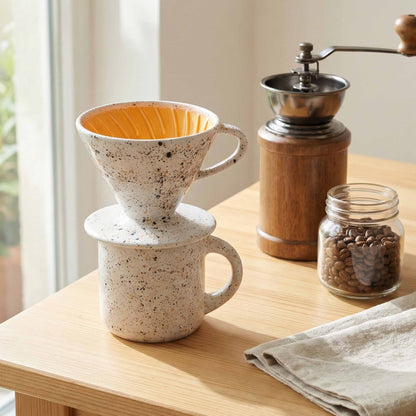 Coffee brewing setup with a ceramic filter, wooden grinder, and jar of coffee beans on a wooden table.