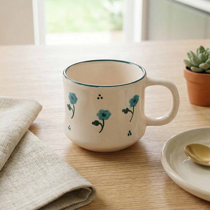 White mug with floral design on a wooden table with a plate and spoon.