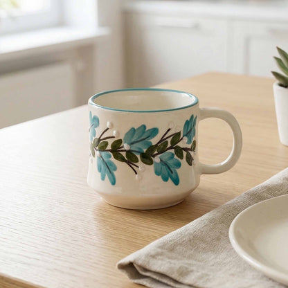 White mug with blue and green leaf design on a wooden table