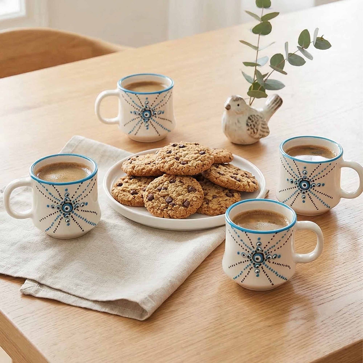 Four mugs with blue patterns filled with coffee, a plate of cookies on a wooden table.