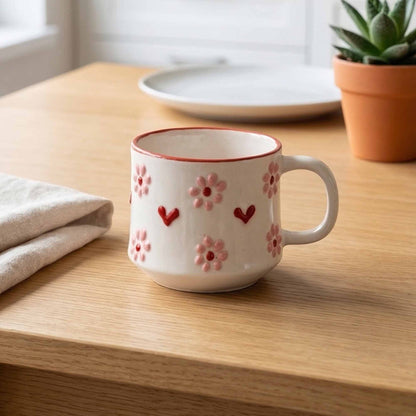 White mug with floral and heart designs on a wooden table with a plant in the background