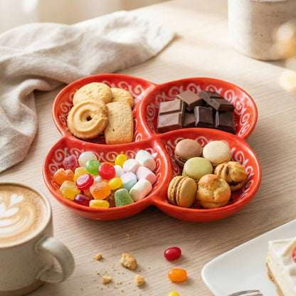 Red divided tray with cookies, chocolates, candies, and macarons on a wooden table with a cup of coffee.