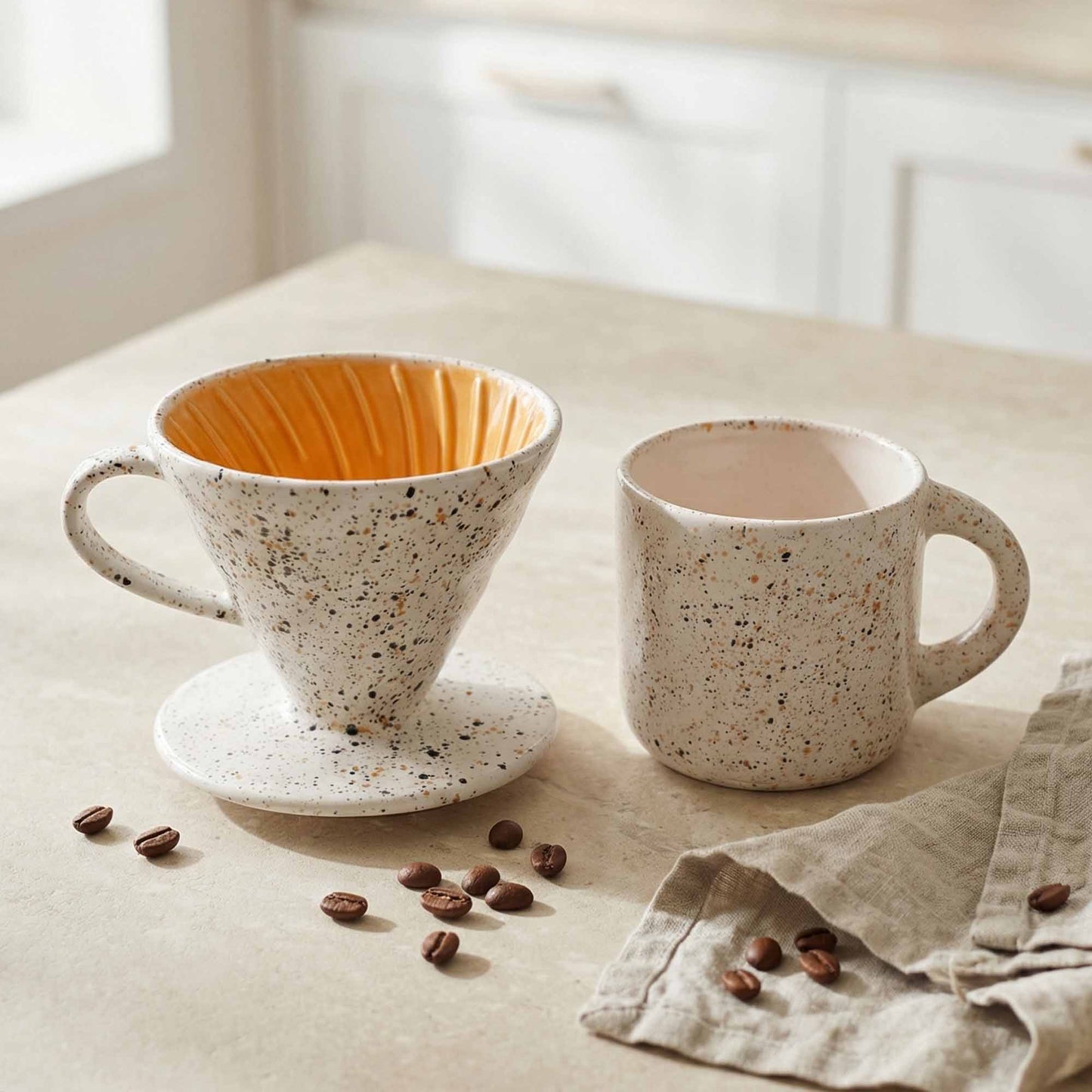 Speckled ceramic coffee filter and mug on a light surface with scattered coffee beans.