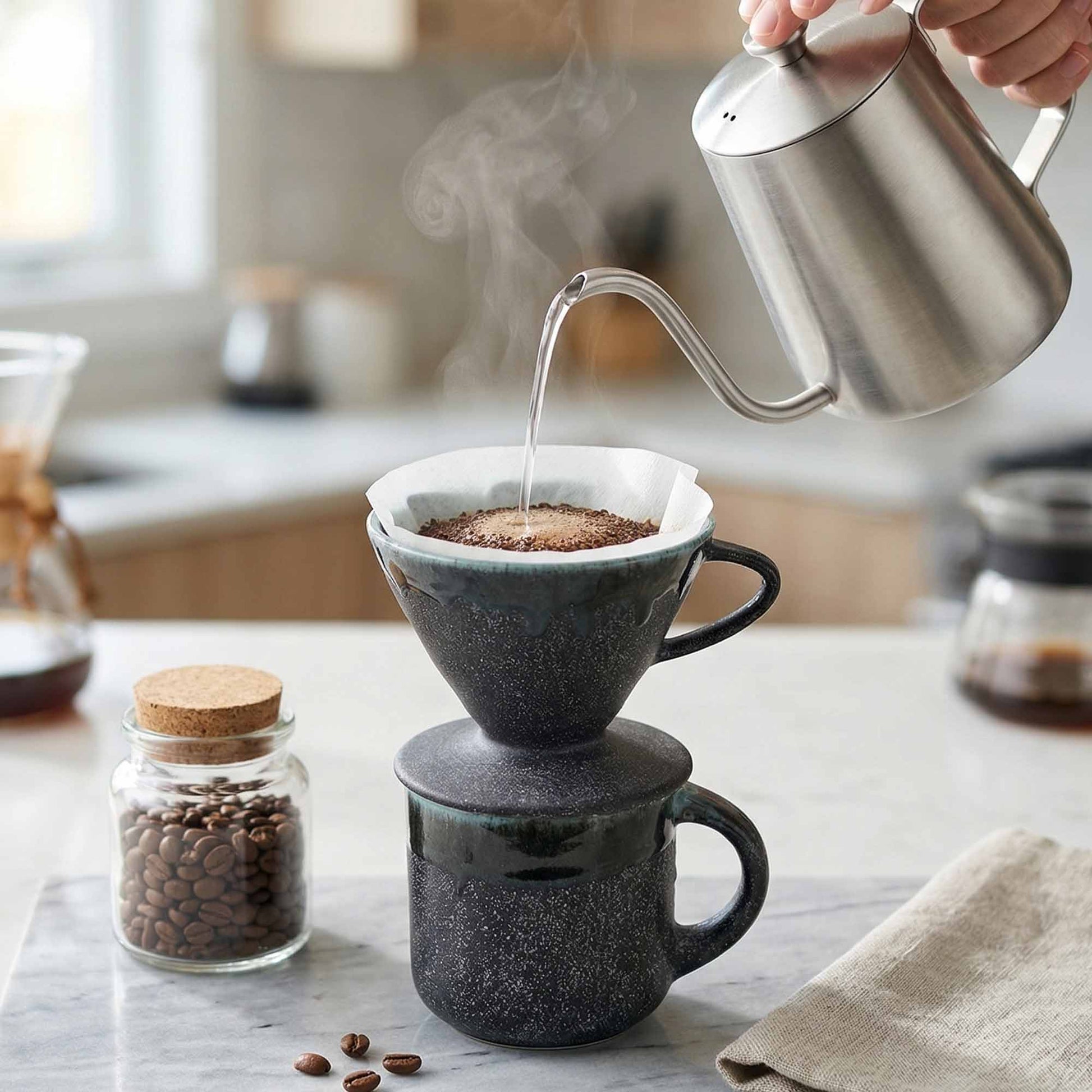 Person pouring steaming water from a kettle into a coffee filter on a mug, with coffee beans and a jar of beans in the background.