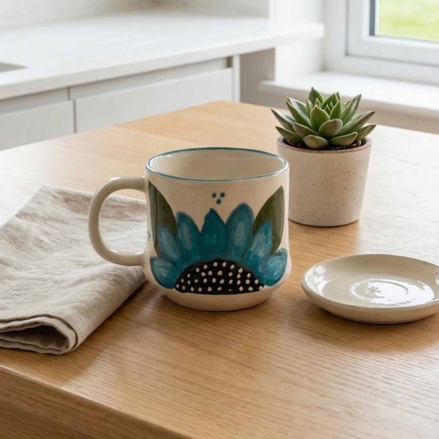 Ceramic mug with floral design on a wooden table, next to a potted plant and small dish.