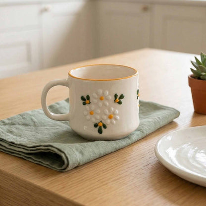 Decorative ceramic mug with floral design on a wooden table with a green cloth and small plant.