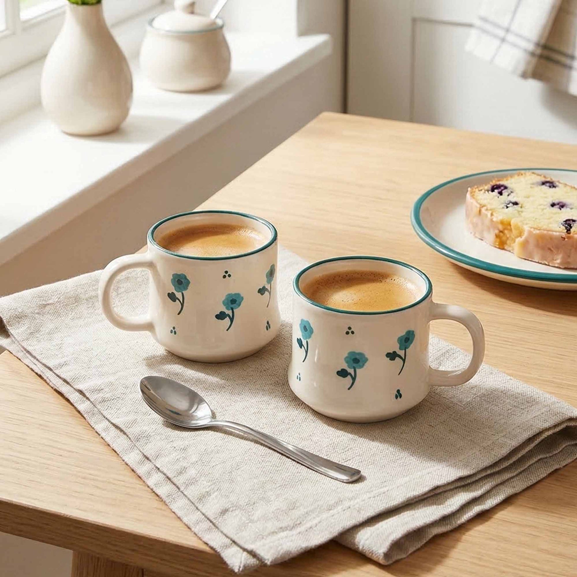 Two floral mugs with coffee on a wooden table with a plate of pastries.